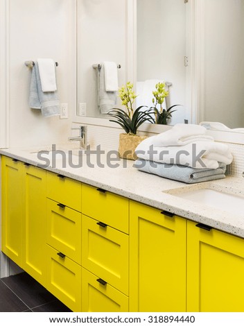 Bathroom detail in new luxury home: colorful yellow vanity with cabinet, mirror, counter, sink, and faucet, decorated with towels