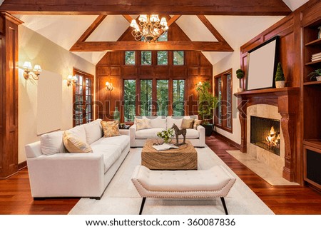 Beautiful living room interior with hardwood floors and fireplace in new luxury home. Includes chandelier, vaulted ceilings, and view of trees through windows.