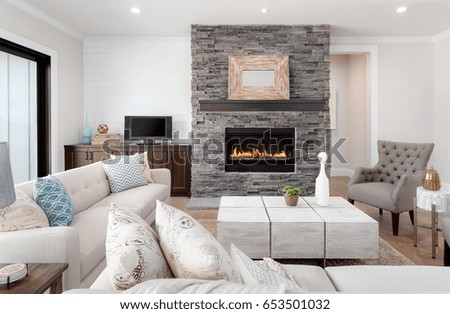 Beautiful living room interior with hardwood floors and fireplace in new luxury home. Couches at right angles face armchairs and fireplace surround stretches to ceiling and is bordered by credenza.