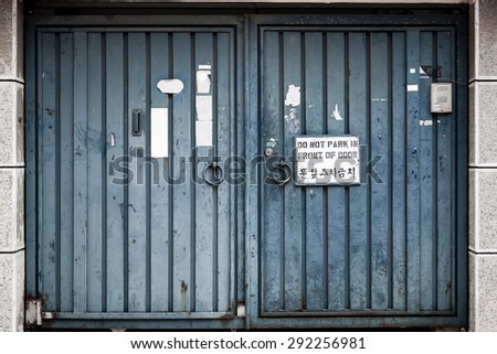 Very weathered and abused metal blue double doors with a sign, \