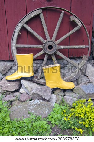 yellow rubber boots near old horse carriage wheel in farm
