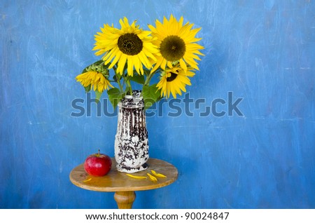 still-life with sunflowers and red apple on blue background