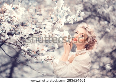 Beautiful blonde with beautiful hairstyle in vintage satin dress in a lush spring garden magnolia