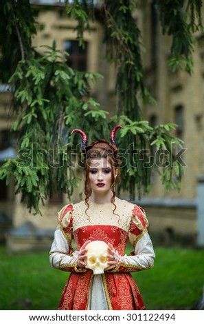 Beautiful girl with demonic horns and skull in his hand, in medieval dress on a background of nature