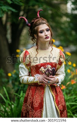 The beautiful girl in medieval dress red with horns, dreaming of something magical