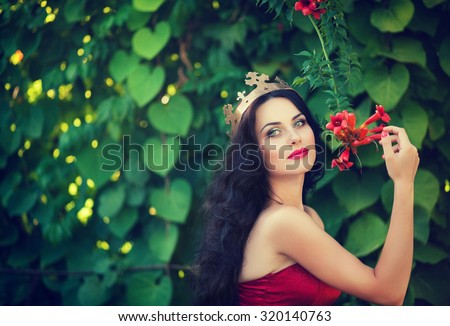Beautiful princess with a golden crown, a red dress and long black hair holding a red flower, walk through the gardens