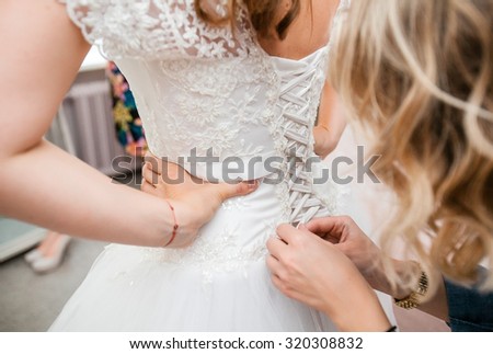 A friend helps a bride corset lace wedding dress