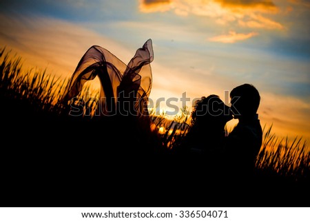 Black silhouettes of men and women against the background of a beautiful sunset, love, dating, kiss, the dress  looks like butterfly wings