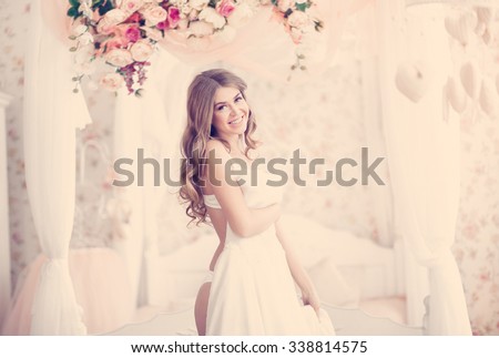 Beautiful blonde bride in the morning of the wedding day in her dress trying on wedding dress the bed with a beautiful canopy decorated with garlands of roses