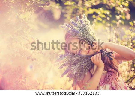 Cute little girl presses to face with two bunches of purple lavender and smiles coyly, family vacation in the park