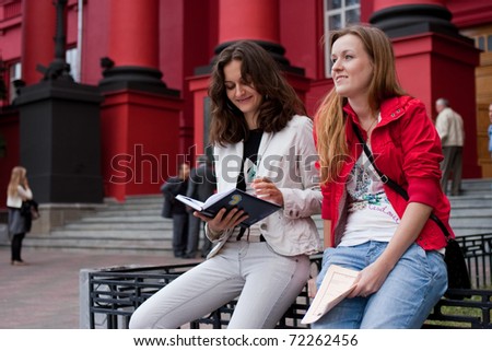 Two students sitting near the red building University Shevchenko in Kiev and read notes.