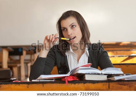 Dark-haired female student sitting at a desk and biting pen.