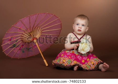 A little girl with a pink Chinese umbrella, studio portrait on a brown background