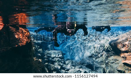 People Snorkeling swimming diving in the blue cold glacier water in famous fissure Silfra between two tectonic plates in the national park Thingvellir in Iceland. Blue transparent water, deep colors.