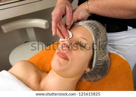 A woman\'s face is cleaned with a wad of cotton wool in a beauty salon