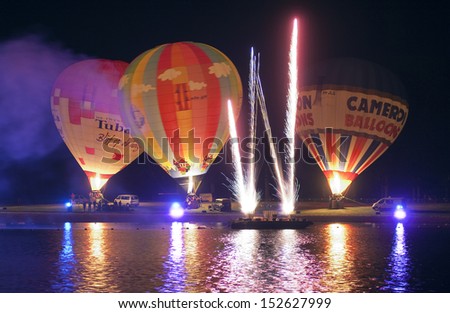 OLDENZAAL, THE NETHERLANDS - AUGUST 23: Seven hot air balloons are glowing on the beach of a recreation pond, with fireworks in front at a festival in the Netherlands, Aug 23, 2013.