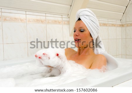A woman is playing with foam and enjoying a hot bath with a towel around her hair