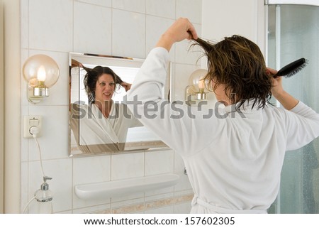 A woman is looking in the mirror of the bathroom and having a \'bad hair day\'.