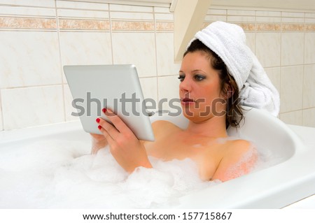 A woman is playing with her tablet while she is enjoying a hot bath