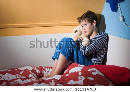 A young boy is sitting afraid and depressed on his bed in his bed room