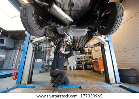 ENSCHEDE, NETHERLANDS - DEC 13: A mechanic is checking the exhaust of a car who is lifted up in a repair service station, December 13, 2013 in the Netherlands