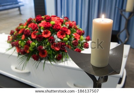 A coffin with a flower arrangement in a morgue and a burning candle in front
