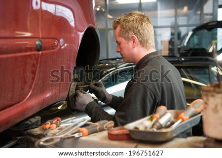 A mechanic in a garage is checking and repairing the brakes of a lifted car.