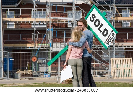 Young couple with blueprint is happy in front of their new built house they just bought