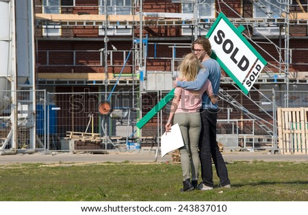 Young couple with blueprint is happy in front of their new built house they just bought
