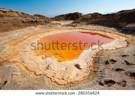 Sinkhole or open pit with orange salty water on the shore\'s of the dead sea at the end of the summer when the water level is at it\'s lowest