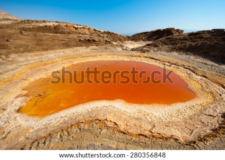 Sinkhole or open pit with orange salty water on the shore's of the dead sea at the end of the summer when the water level is at it's lowest