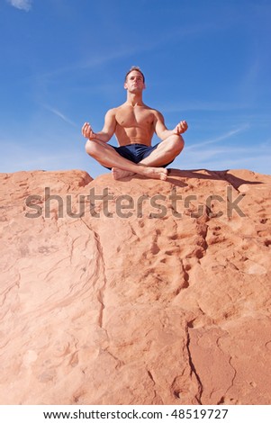 Muscular man meditating on red rocks