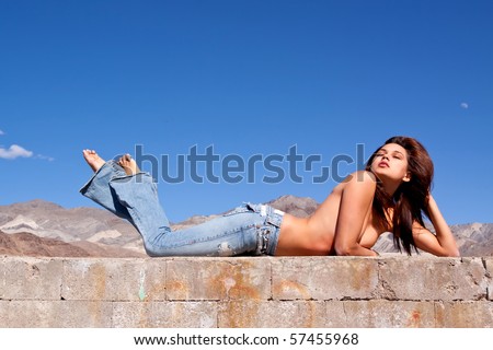 Gorgeous young brunette woman sun tanning on a concrete wall