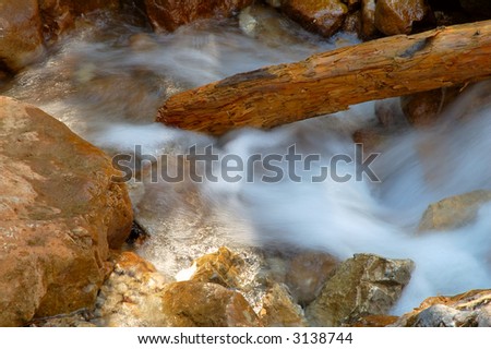 Log in creek water among rocks frozen in time
