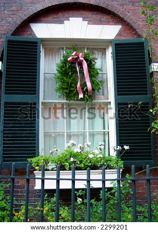 beautiful arched window frame with shutters and christmas wreath, flower box and old wrought iron fence in boston on beacon hill