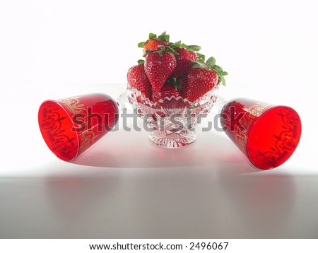 Crystal bowl filled with strawberries including red glasses on a white background.