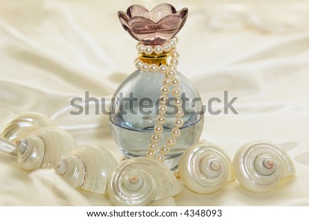 Beautiful blue ornate oval shaped tinted glass perfume strung with pearls on a white satin background.