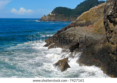 beautiful dramatic scenic image of the waves crashing upon the rocky coast with light house in the background