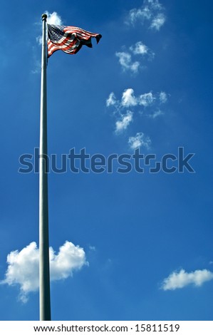 american flag blows in the wind at the top of a white flag pole against a rich blue sky