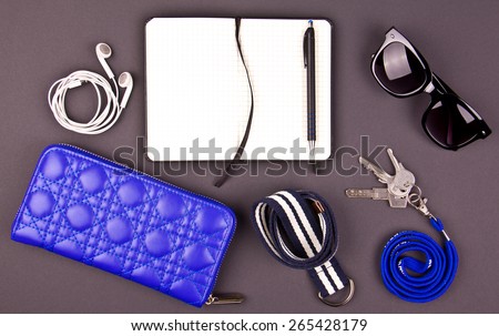 Conceptual still life of random objects of modern human. Keys, wallet, sunglasses, earphones, striped belt, paper notepad, pen. Dark gray background. Aerial view.