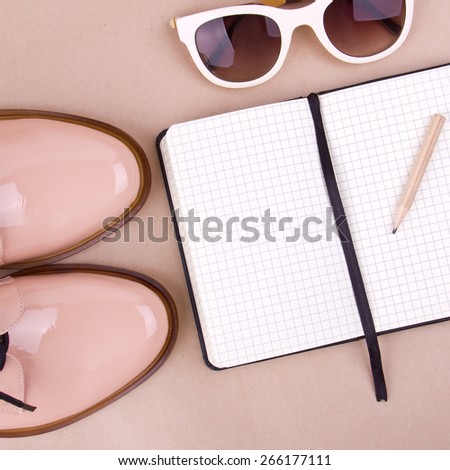 beige patent leather shoes, white sunglasses, small paper notebook with a pencil, beige background. Place for your text.