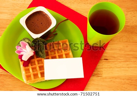 Waffle, chocolate mousse and juice, decorated with flowers and blank ticket placed on plate.