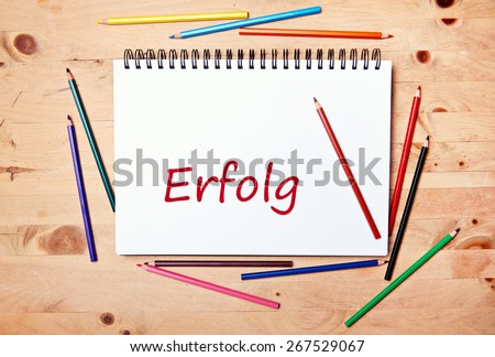writing pad on wood table with colored pencil - german for success