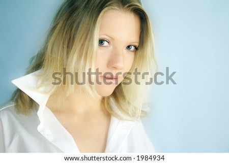 A young blond woman is wearing a shirt of a man and is smiling in the camera
