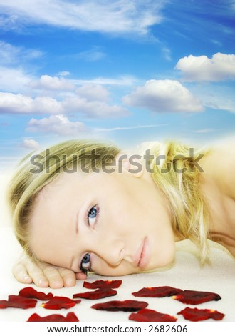 a fresh and beautiful blond woman laying on a yellow towel with flowers and in front of the blue sky