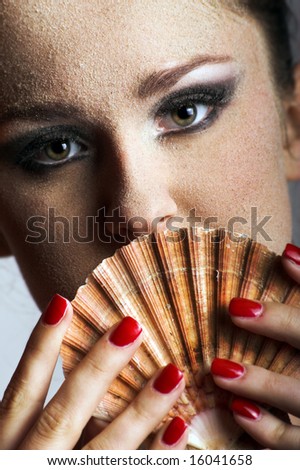 Beauty portrait of a young beautiful woman with sand on her skin and a shell