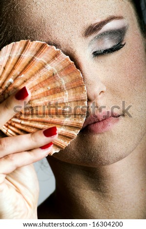 Beauty portrait of a young beautiful woman with sand on her skin and a shell