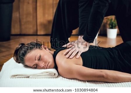 Beautiful young sporty woman enjoying shiatsu back massage, lying on the wooden floor, wearing black top