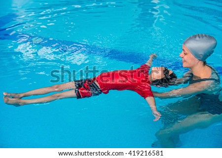 Swimming lessons for children - Swimming instructor helping little boy to relax in water