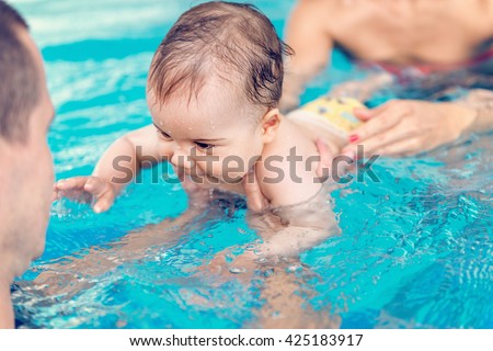 Cute baby boy swimming with instructor and his mother in the pool
